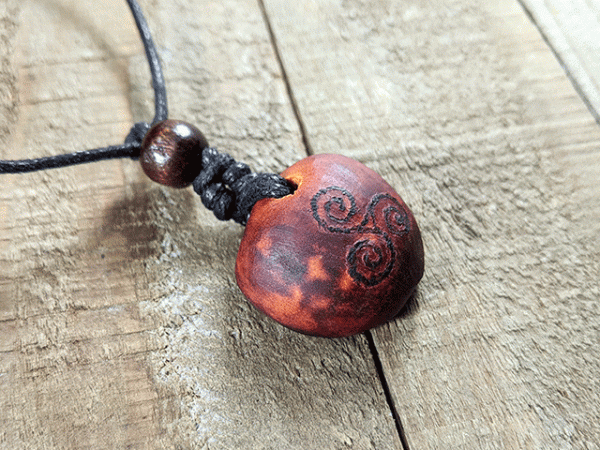 hand-carved avocado stone necklace with burned triskelion pattern